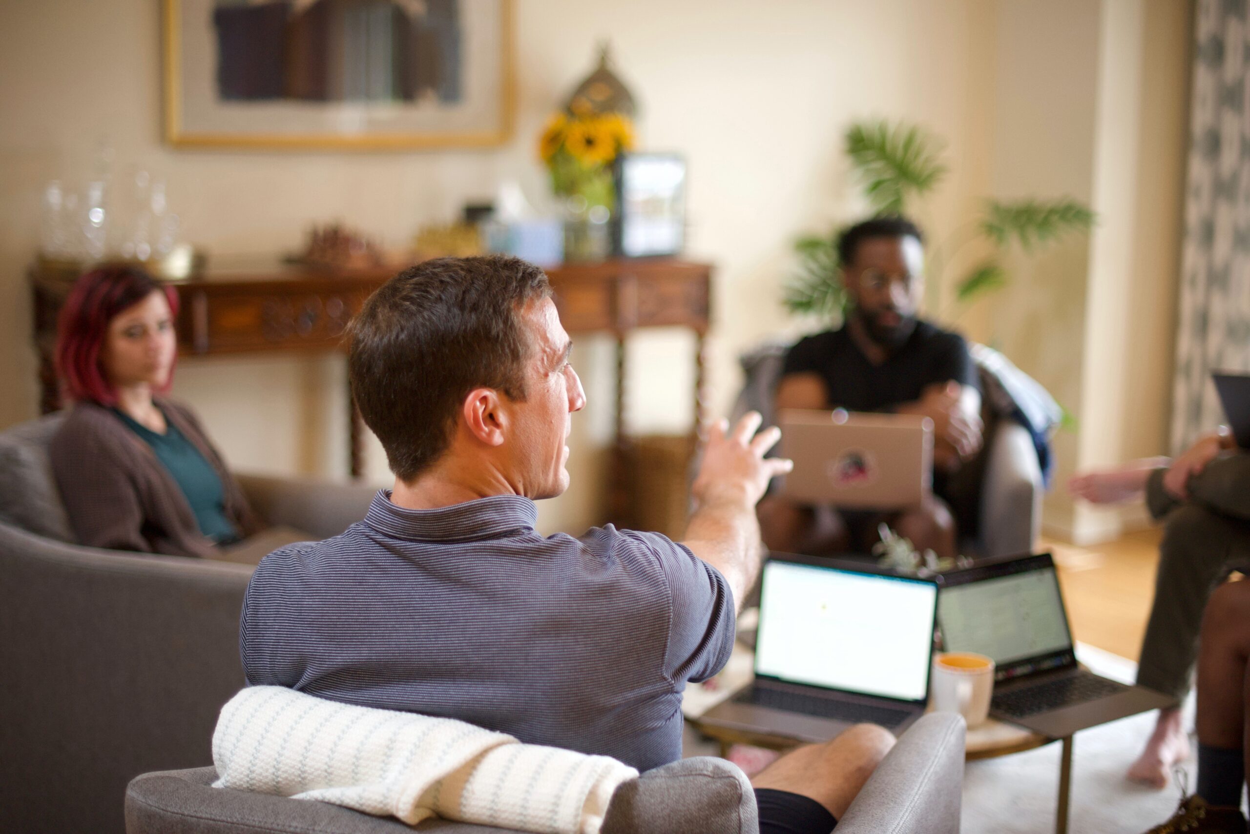 Two men and one woman sit on armchairs with laptops in front of them, in a meeting in a residential lounge
