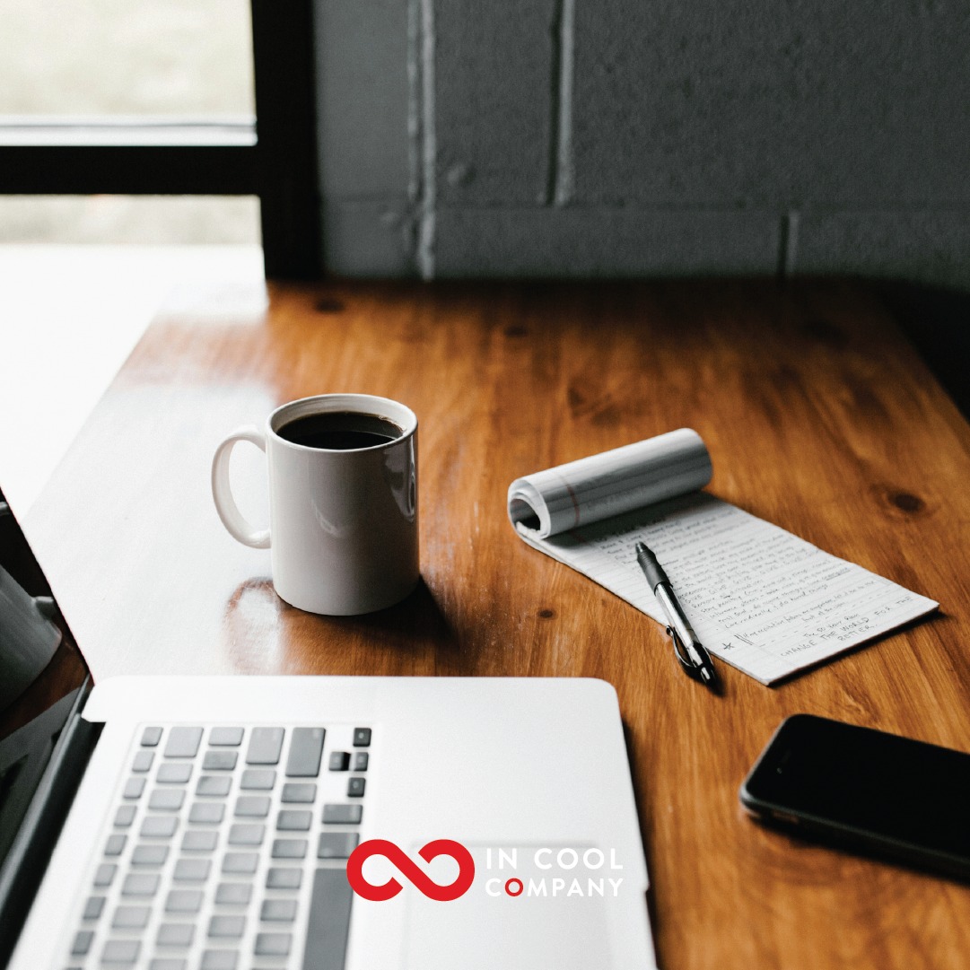 An open laptop, a mobile phone, and a notepad sit on top of a desk