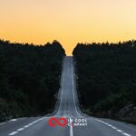 A long straight, undulating road, flanked by forests, disappears over the brow of a hill