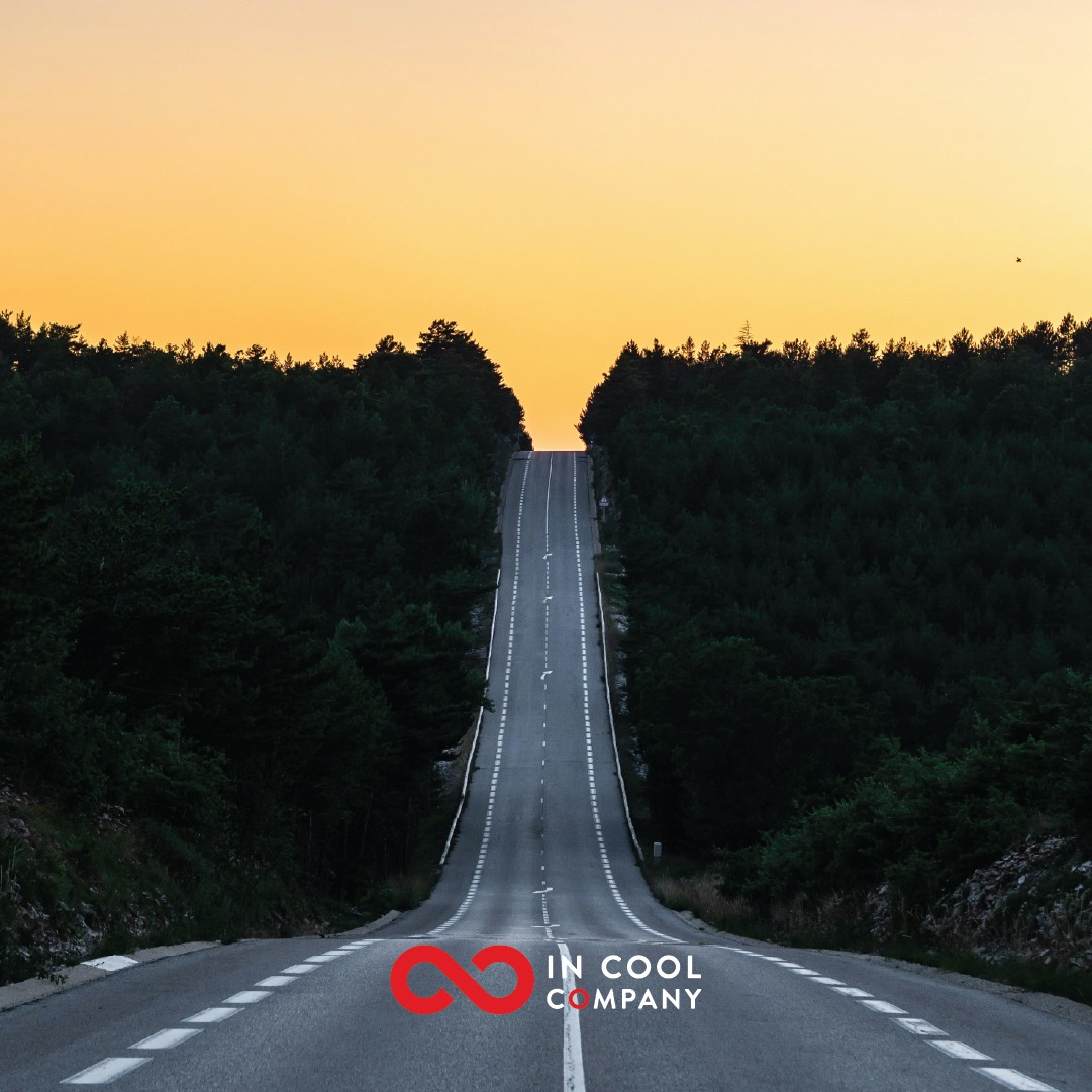 A long straight, undulating road, flanked by forests, disappears over the brow of a hill