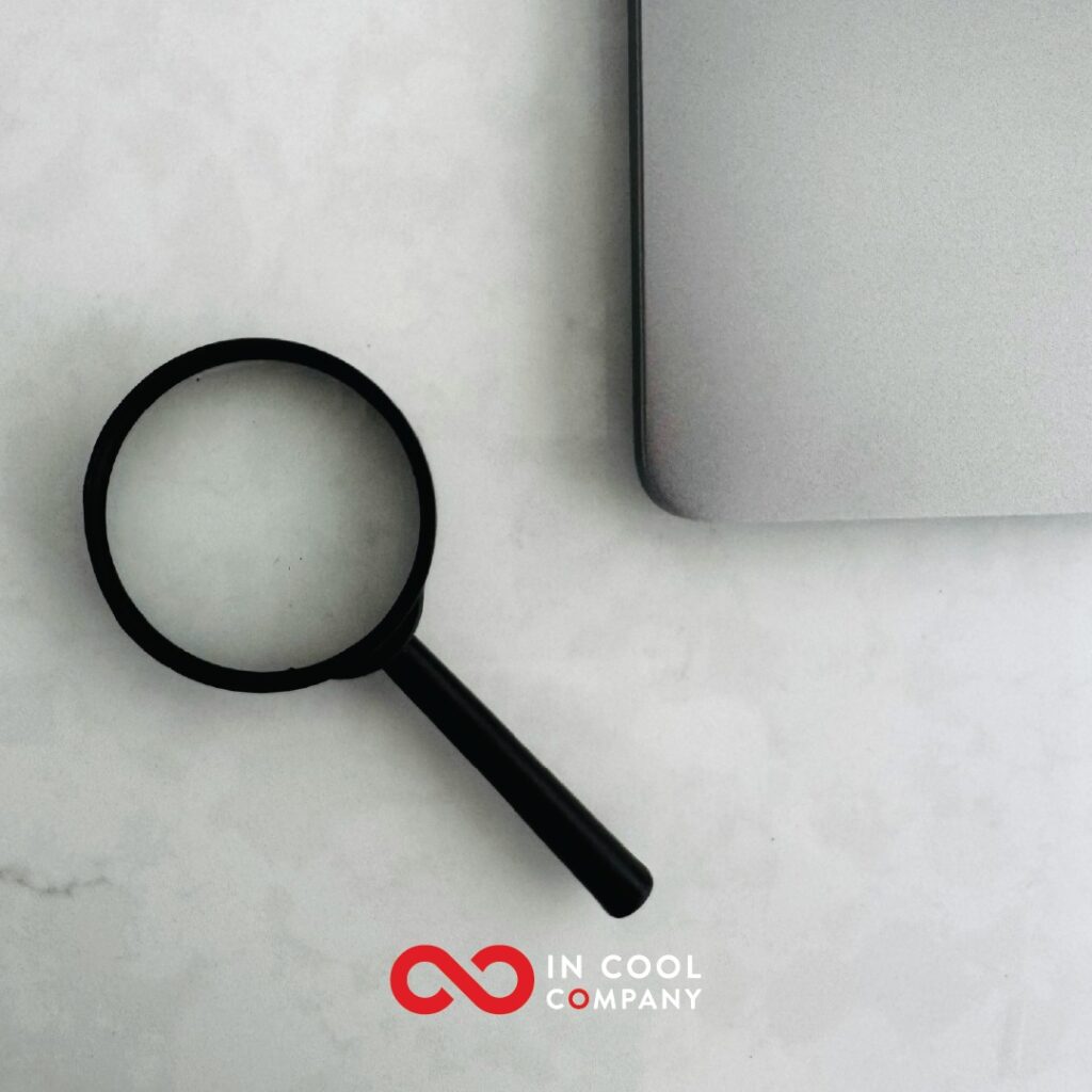 A magnifying glass lies in a table next to a laptop