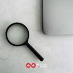 A magnifying glass lies in a table next to a laptop