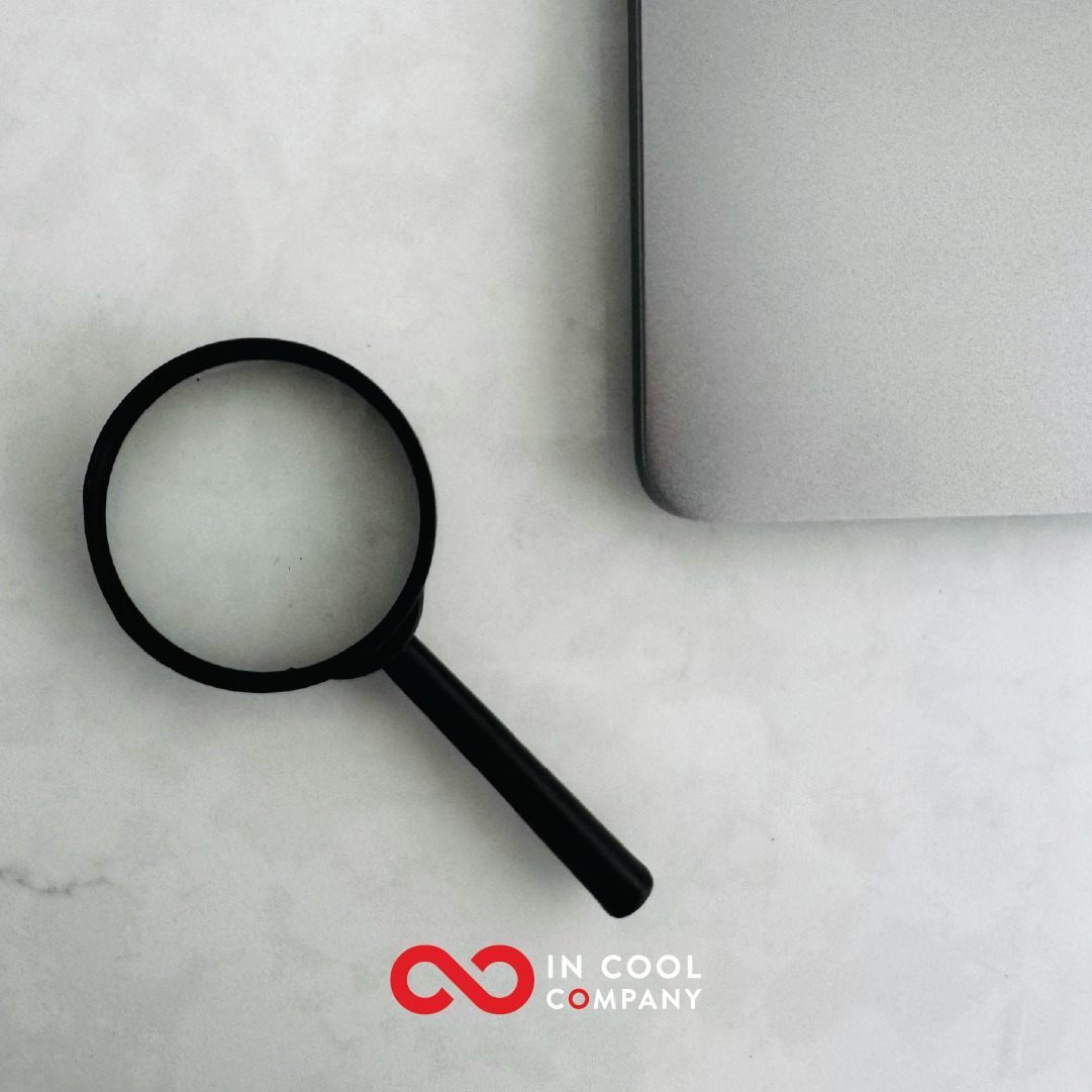 A magnifying glass lies in a table next to a laptop