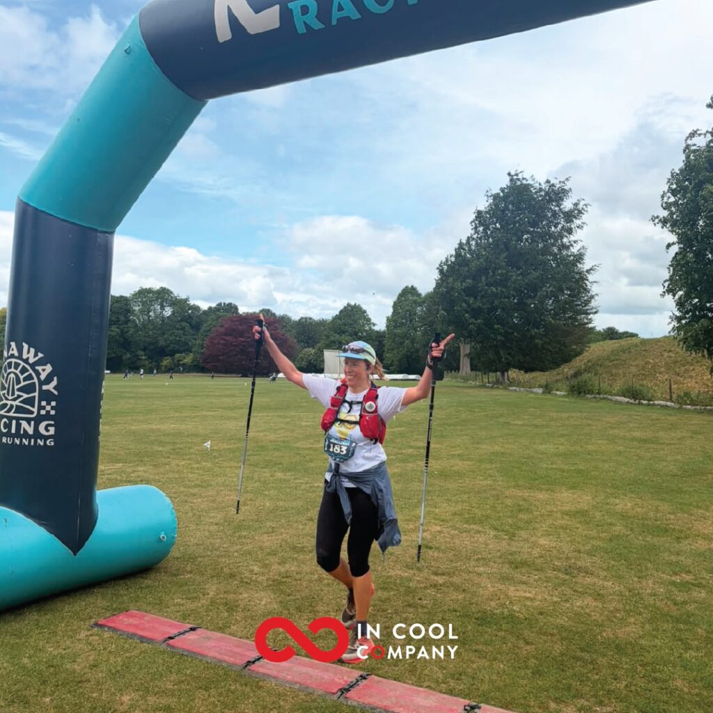 A female crosses a finish line on foot with arms raised in the air