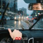 A man drives a car looking through a dirty, wet windscreen