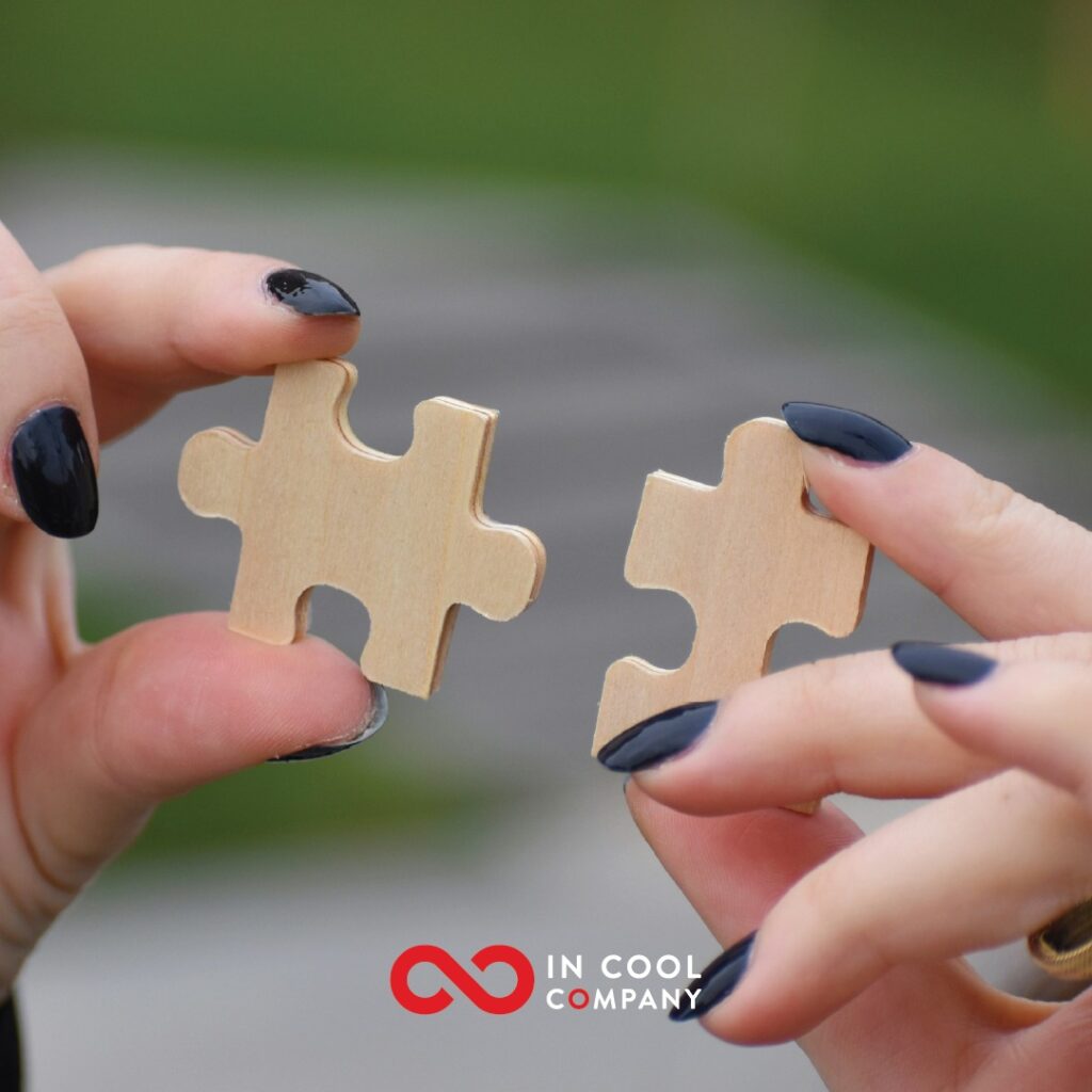 Two different jigsaw puzzle pieces are held out by a woman's hands
